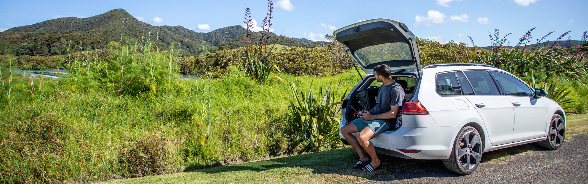 Young man sitting at the boot of his car enjoying a scenic view