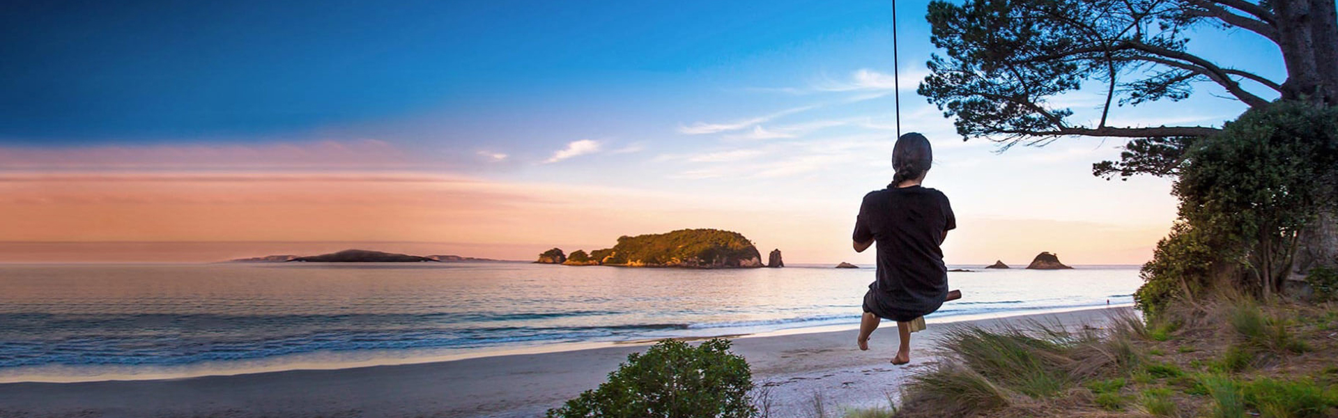 A young person on a rope swing overlooking a calm ocean.