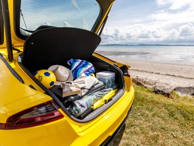 Yellow car parked at the beach with a boot full of beach gear.