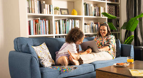 Daughter and mum with laptop relaxing on the couch.