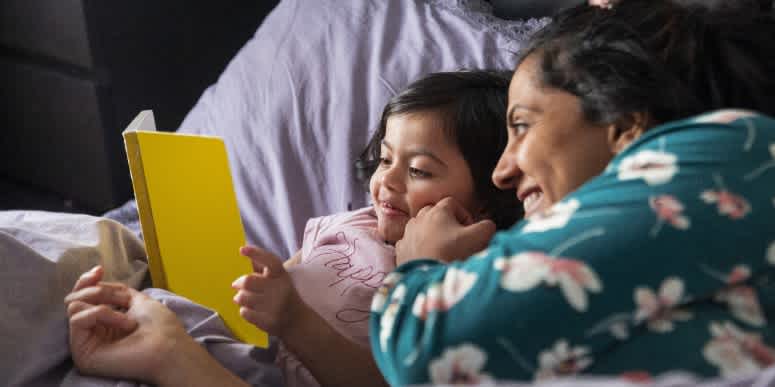 Image of a mother and child in bed reading a book.