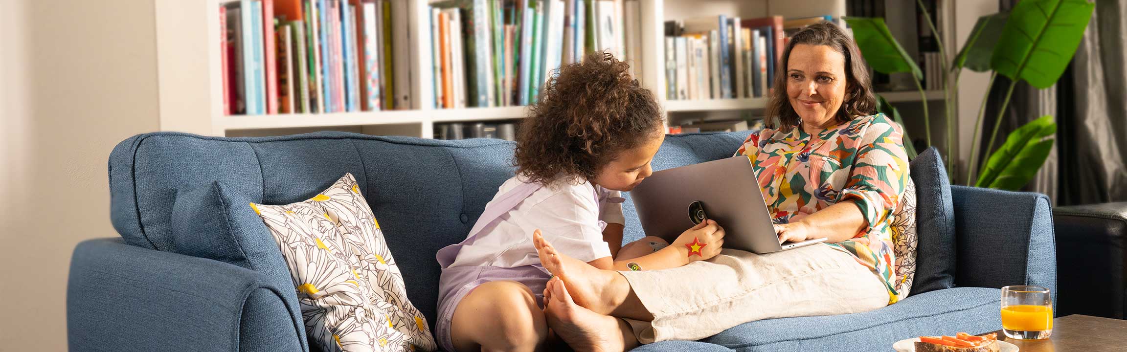 Mum works on laptop on the couch while daughter sits by her legs