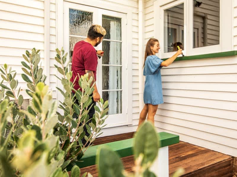 Two people are maintaining their property by painting the outside of the house.