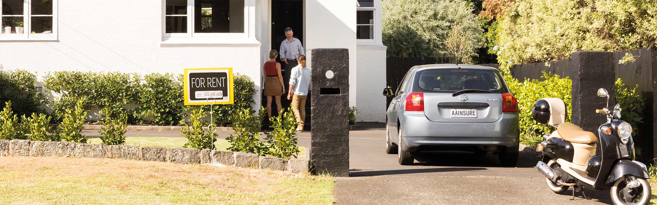 A house with a "for rent" sign and a man leading a couple inside