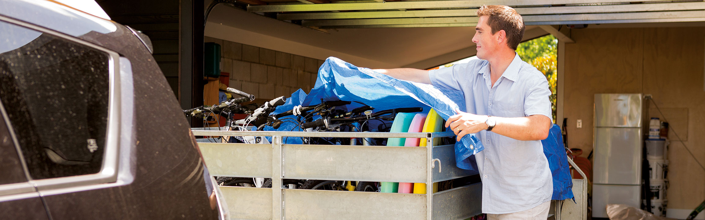 A man covering his trailer holding bikes and body boards